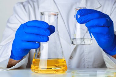 Mavi eldivenli bilim adamı ya da doktor bir mataraya sarı sıvı döküyor.