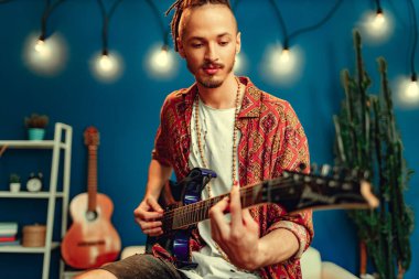 Evde gitar çalma alıştırması yapan havalı bir adam.