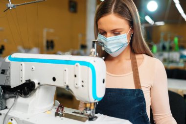 Korumacı tıbbi maske takarak dikiş fabrikasında çalışan beyaz kadın terzi.