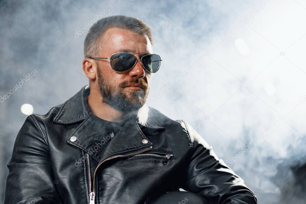 Portrait of bearded man motocyclist in dark sunglasses on dark background
