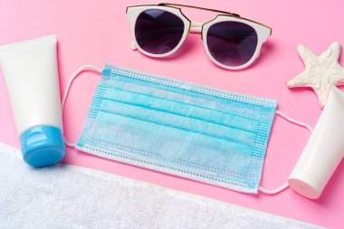 Pembe arka planda güneş kremi olan tıbbi maske. Coronavirus yaz konsepti
