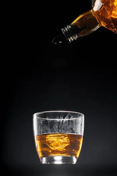 Whisky derramando em um copo no fundo preto — Fotografia de Stock