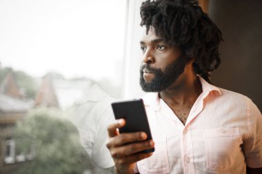 Sakallı genç Afrikalı Amerikalı adam akıllı telefonuna bakıyor.