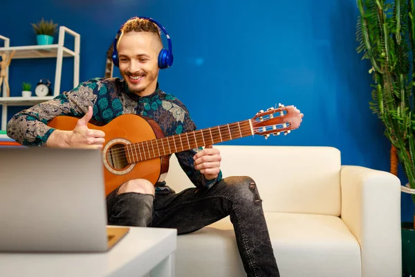 Young stylish caucasian man taking guitar class online at home using his laptop