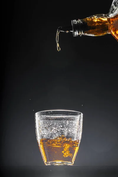 Whisky derramando em um copo no fundo preto — Fotografia de Stock