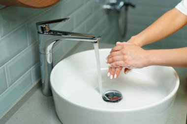 Ellerini banyo lavabosunda yıkayan bir kadının yakın çekimi.