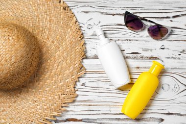 Hasır şapka, güneş gözlüğü ve tahta arka planda güneş kremi şişesi.
