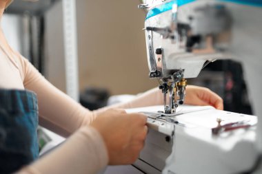 İşyerindeki terzi kadın dikiş makinesine kıyafet dikiyor.