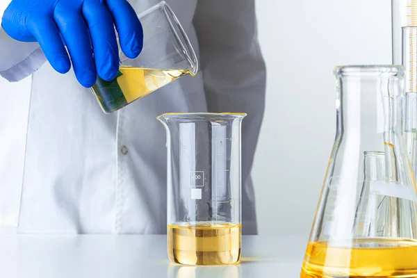 Wissenschaftler oder Arzt in blauen Handschuhen gießt etwas gelbe Flüssigkeit in einen Kolben — Stockfoto
