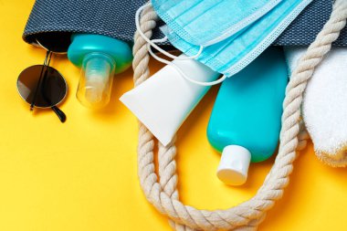 Plaj aksesuarlarıyla mavi kumsal çantası ve sarı arka planda koruyucu maske.