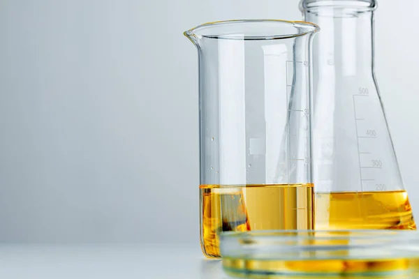 Artículos de vidrio de laboratorio con líquido aceitoso amarillo sobre fondo gris — Foto de Stock