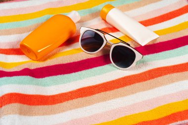 Pembe ahşap arka planda güneş kremi ve güneş gözlüklü renkli çizgili havlu.