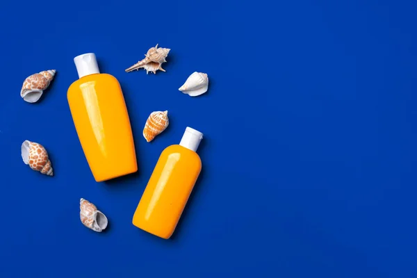 Botellas con bloqueador solar cosméticos y conchas marinas sobre fondo azul oscuro — Foto de Stock