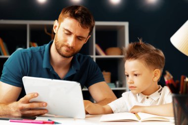 Genç çocuk babasıyla masada oturuyor ve dizüstü bilgisayar kullanıyor.