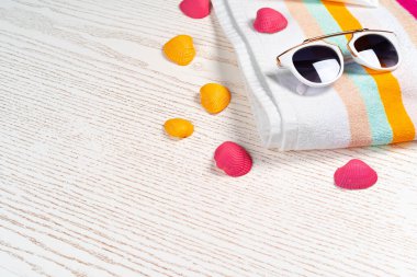 Güneş gözlüğü ve tahta üzerinde deniz kabukları olan renkli çizgili havlu.