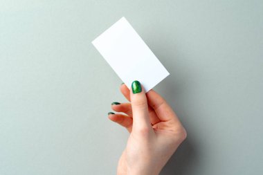 Manikürlü bir kadın eli masanın üzerinde beyaz kartviziti tutuyor.