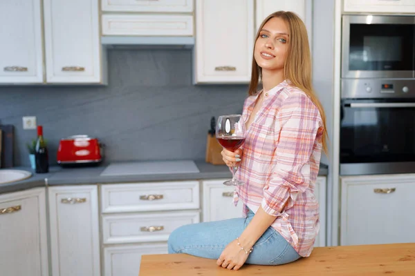 Mulher branca loira com copo de vinho tinto em pé em sua cozinha — Fotografia de Stock