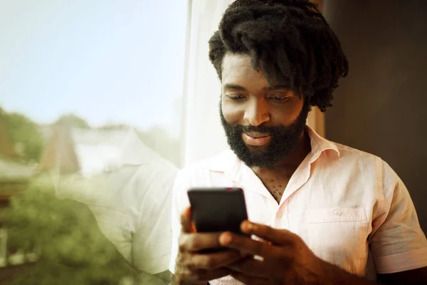 Sakallı genç Afrikalı Amerikalı adam akıllı telefonuna bakıyor. — Stok fotoğraf