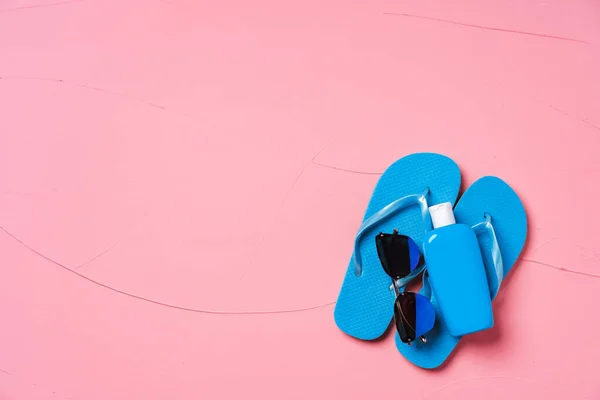 Chanclas azules con protector solar y gafas de sol sobre fondo rosa — Foto de Stock