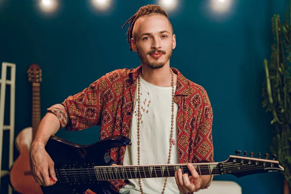 stock image Young man guitar player sitting and performing on a couch