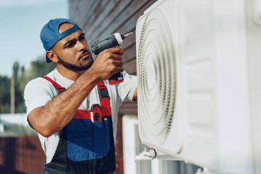 Repairman in uniform installing the outside unit of air conditioner clipart