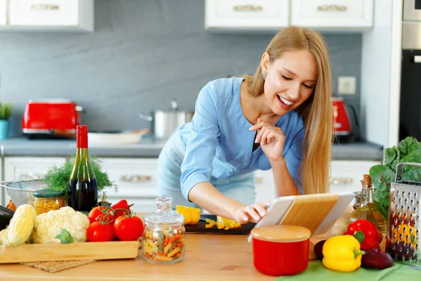 Jovem bela mulher caucasiana cozinhar e usar seu tablet digital na cozinha — Fotografia de Stock