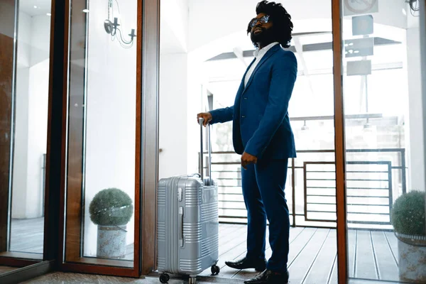 Svart man i formell kostym med packad resväska kommer in hotelldörren — Stockfoto