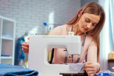 Genç terzi tekstil fabrikasında dikiş makinesi üzerinde çalışıyor.