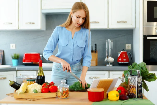 Jovem mulher branca loira cortando legumes para salada em sua cozinha — Fotografia de Stock