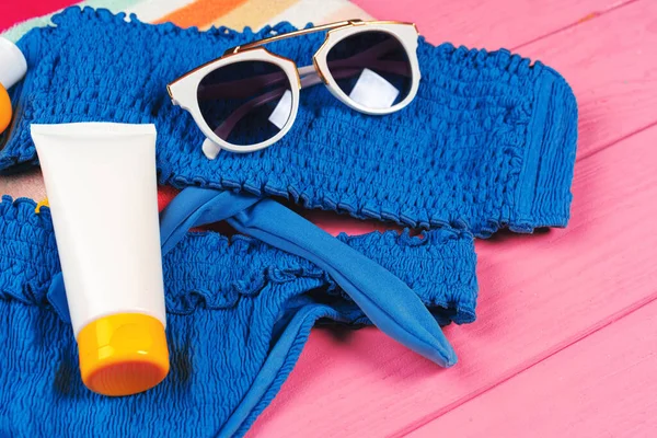 Bikini azul con botella crema bloqueador solar sobre fondo de madera rosa brillante — Foto de Stock