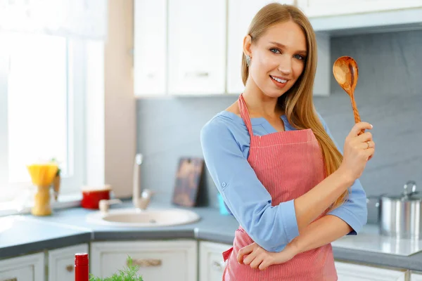 Atractiva joven en delantal rojo de pie en su cocina —  Fotos de Stock