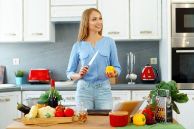Genç, beyaz bir kadın mutfakta yemek pişiriyor ve dijital tabletini kullanıyor.