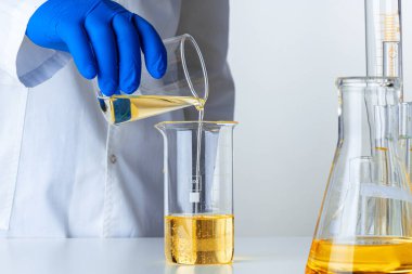 Mavi eldivenli bilim adamı ya da doktor bir mataraya sarı sıvı döküyor.