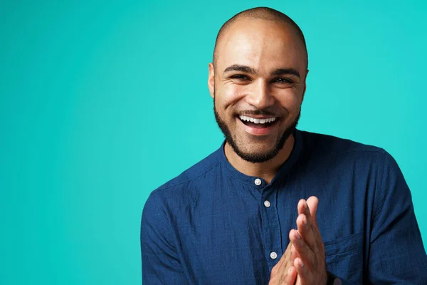 Joyful dark-skinned man laughing against turquoise background