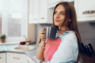 Kırmızı önlüklü güzel bayan mutfağında bir fincan kahvenin keyfini çıkarıyor.