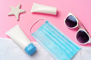 Pembe arka planda güneş kremi olan tıbbi maske. Coronavirus yaz konsepti