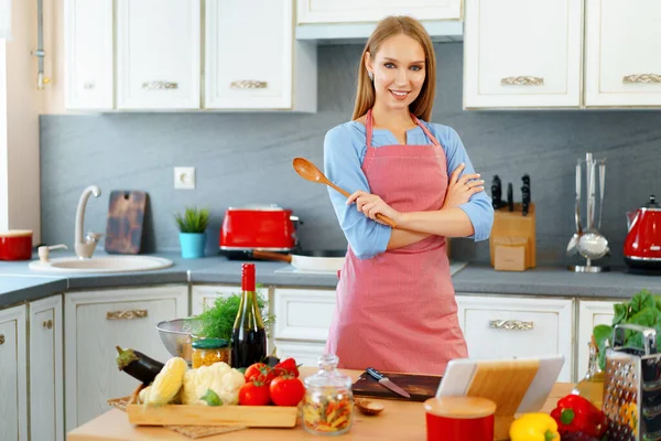 Atractiva joven en delantal rojo de pie en su cocina —  Fotos de Stock