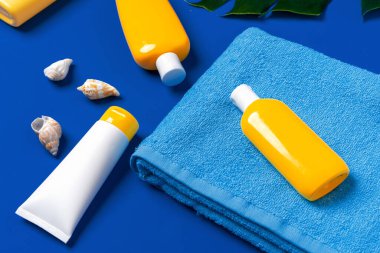 Güneş kremli şişeler ve koyu mavi arka planda deniz kabukları.