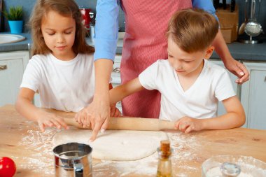 Genç sarışın kadın, anne ve çocukları hamur pişirirken eğleniyorlar.