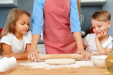 Anne ve küçük çocukları, kız ve erkek, mangırı hazırlamasına yardım ediyorlar.