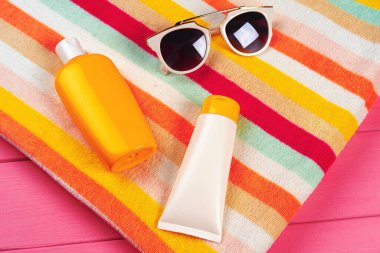 Pembe ahşap arka planda güneş kremi ve güneş gözlüklü renkli çizgili havlu.