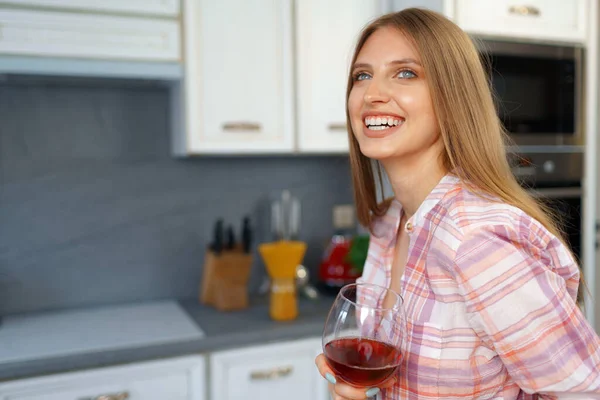 Mulher branca loira com copo de vinho tinto em pé em sua cozinha — Fotografia de Stock