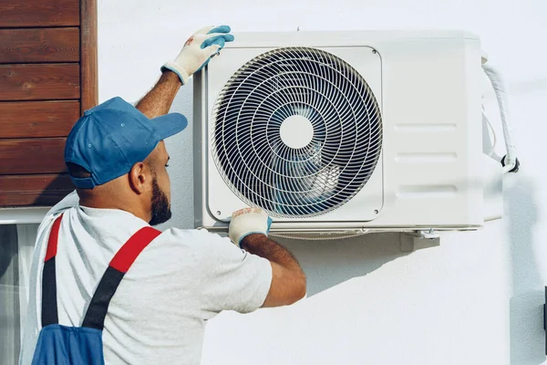 Repairman in uniform installing the outside unit of air conditioner — Stock Photo, Image