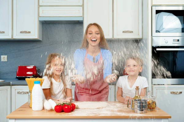 Young blonde woman, mother and her kids having fun while cooking dough — Stock Photo, Image