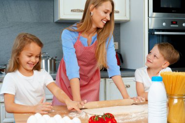Genç sarışın kadın, anne ve çocukları hamur pişirirken eğleniyorlar.