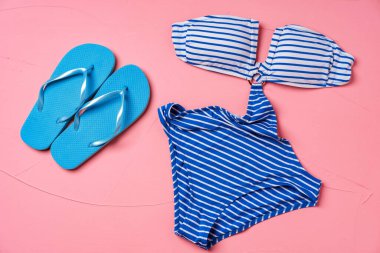 Pembe arka planda mavi parmak arası terlikleri olan mavi çizgili monokini.