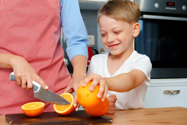 Niño pequeño ayuda a su mamá a cortar naranjas — Foto de Stock