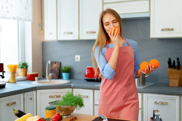 站在厨房时，穿着红色围裙的美丽的高加索女人拿着成熟的橙子 — 图库照片