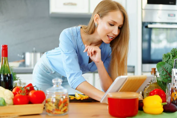 年轻美丽的高加索女人在厨房做饭和使用她的数码平板电脑 — 图库照片