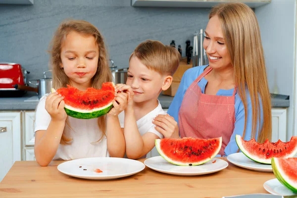 Słodka rodzina, matka i jej dzieci jedzą arbuza w kuchni i dobrze się bawią — Zdjęcie stockowe